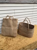 Two woven bags grouped together outdoors on a surface against a siding wall, showing the overall size and shape difference.