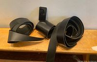 Black leather belt strips rolled and stacked on a shelf, with a small black item standing upright for scale.