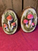 Pair of oval chalkware mushroom motif plaques on red cloth background with wood wall