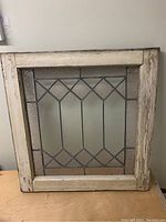 Full view of the antique stained glass panel in square wood frame with distressed paint and geometric design glass.
