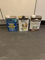 Three cans of furniture oils on floor showing brands and condition