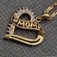 Close-up of 10kt gold heart pendant inscribed ‘MOM’ with diamond accents