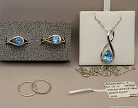 Infinity pendant necklace, stud earrings, and rings displayed on grey background