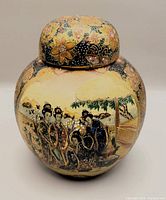 Front view of small hand painted Japanese satsuma porcelain ginger pot with lid, depicting a traditional scene with Japanese figures and floral decorations.