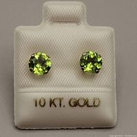 Close-up of earrings on white display showing 10kt gold stamp and round green peridot stones