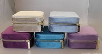 Five velvet jewellery boxes stacked in two rows showing closed lids in beige, burgundy, teal, light blue and light purple colors with LA KAISER zipper pulls shown