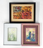 Three original watercolor paintings displayed together, each framed and matted showing abstract, farm building, and floral subjects.
