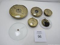 Top-down photo of 4 round barometers with convex glass covers and one loose convex round glass cover, all laid flat on white background, with lot number card visible