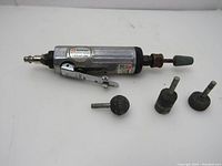 Side view of the metal die grinder with attached air hose connector and four grinding bits arranged next to it on a white surface.