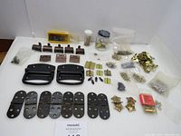 Overview of entire lot showing black tool box handles, multiple hinges, brass picture hangers and hooks, and bags of small nails and screws.