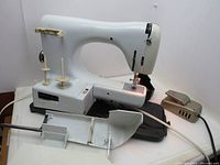 White Necchi Lydia Type 544 sewing machine sitting on a surface with foot pedal behind it. Power cord visible with electrical tape on wire.