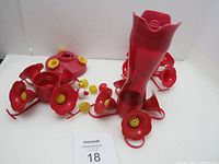 Photo showing assembled red plastic hummingbird feeder with multiple yellow feeding ports and base along with extra parts laid next to it.