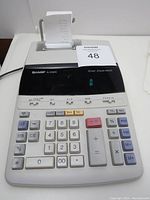 Full view of SHARP EL-2192RII calculator showing 12-digit green fluorescent display, keypad, and built-in two-color serial printer with paper roll.