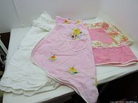 Three vintage aprons displayed lying flat: pink floral embroidered apron with pocket, pink reversible apron with floral backing, and plain white apron.