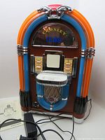 Front view of Crosley CR17 Mini Victrola style jukebox with remote and instruction manual partially visible at base.