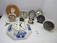Wide shot of all 10 clocks arranged on table showing variety of sizes, shapes, and materials.