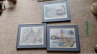 Three framed watercolor artprints on carpet showing San Francisco Bay scenes including bridge, cable car, and hillside