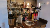 Assorted glassware on mirrored shelves including wine glasses, martini glasses, and goblets with various bar accessories on a counter with sink