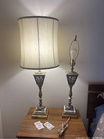 Pair of vintage table lamps on wooden table, one with off-white fabric shade lit, other without shade.