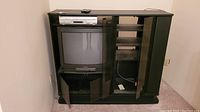 Full view of black wooden entertainment stand with glass doors housing a black Toshiba box TV and a silver Sony combo VHS/DVD player on top shelf.