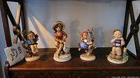 Four ceramic Hummel figurines arranged on a shelf, showing all pieces in the lot