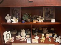Full shelf with porcelain Cherished Teddies figurines, collectible teddy bears, ceramic décor items, small angel figurines, and miniature baby shoes.