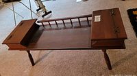 Brown wooden coffee table front view showing hinged lids on side storage compartments and turned legs.