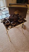 Photo showing a foldable TV tray with the brown ceramic soup tureen and six matching bowls arranged on top, all placed on a carpeted floor.