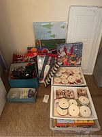 Photo showing assorted Christmas-themed gift bags, boxes, and some ribbons in a box on carpeted floor.