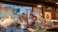 Multiple glass and ceramic decorative items displayed including teapots, plates, vases, and creamers with floral motifs