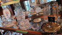 Full view of multiple glass and ceramic decor items on mirrored surface including pedestal cake stand, various plates, and a large ceramic floral dish.