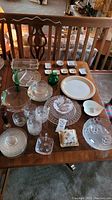Full table layout of glass and crystal serving dishes, plates, bowls, colored glass vases, small decorative dishes, and drinking glasses