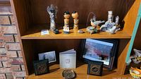 Wide view of wood shelf with various figurines on top shelf, photo frames and small dish on middle shelf