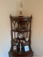 Shelf with oil lamp on top and items on shelves including shoe flower holder, decorative plate, glass bottle, picture frames, and candle holder