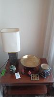 Table lamp, brass bowl, snuff bottles, good luck trivet and urn arranged on a wooden table.