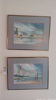 Photo showing two framed original watercolor paintings stacked vertically on wall, with light blue matting and gold frames