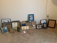 Wide view of assortment of over 25 picture frames arranged leaning against wall showing variety of sizes, finishes, and styles.
