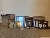 Photo of various picture frames arranged on carpeted floor, showing different sizes and frame styles