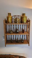 Full view of rattan wall shelf with brass containers on top and six small figurines on lower shelves