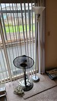 Photo showing the oscillating fan and standing floor lamp side by side near window.