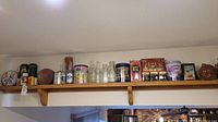 Wide shot of assorted vintage collectors tins and soda bottles on a wooden shelf including round and cylindrical tins and clear glass soda bottles.