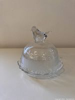 Front view of glass dome with bird topper showing overall shape, clear glass with frosted etching, and scalloped glass plate base.