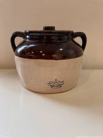 Full view of brown and cream stoneware bean pot with two handles and a lid resting on a white surface.