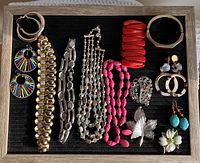 Photo showing a full layout of 12 costume jewelry items: 2 red bracelets, 3 necklaces, 3 brooches, and 4 pairs of earrings arranged on a black background in a wooden frame.