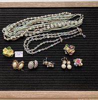 Full lot including necklaces, clip-on earrings, and ceramic floral brooches on black background with light wood frame.