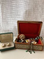 Overview of the costume jewelry lot inside a wooden jewel box with red flocked lining, and a separate green box holding clip-on earrings.