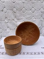 Three handcrafted wooden bowls on a white lace textile backdrop. Larger bowl on the right, two smaller bowls stacked on the left.