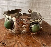 Front view of the silver bracelet showing a large green stone and engraved silver link detail on carved wooden surface.