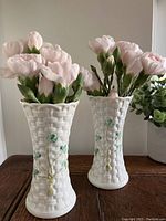 Front view of pair of white Belleek porcelain vases filled with flowers on a wooden surface, showing embossed basket weave and shamrock details.