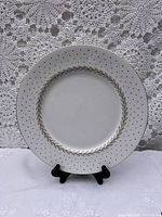 Single dinner plate shown on black stand against crochet lace background, showing gold leaf interior ring, black polka dots and gold rim edge detail.